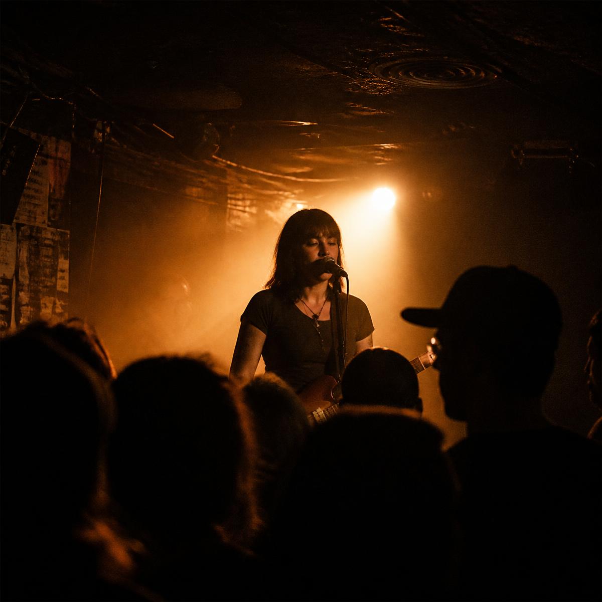 Singer at the mic under an amber spotlight in a small venue